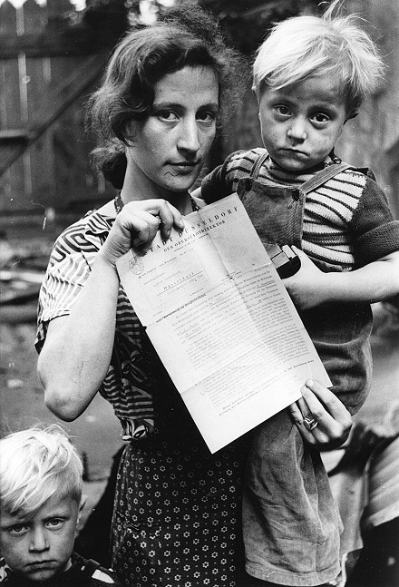 Mutter mit zwei traurig blickenden Kindern hält amtliches Schreiben in der Hand.