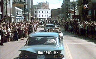 Die Wagenkolonne von John F. Kennedy fährt durch Dallas - kurz bevor Kennedy erschossen wird. Einblendung: 'Um 13:00 Uhr'